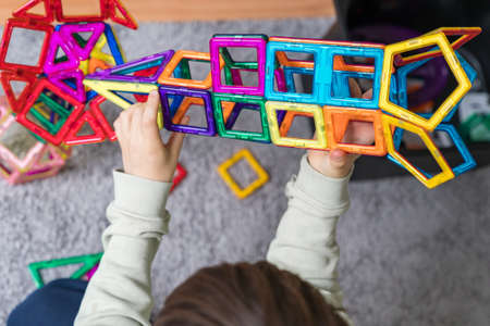 Child plays with a magnetic constructor in a room. Boy building a rocket from blocks. Kid playing with colorful toys.の写真素材