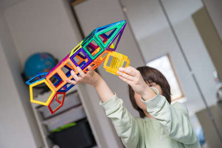 Child plays with a magnetic constructor in a room. Boy building a rocket from blocks. Kid playing with colorful toys.の写真素材