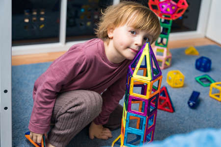 Child plays with a magnetic constructor on a carpet in a room. Boy building a rocket from blocks. Kid playing with colorful toys.の写真素材