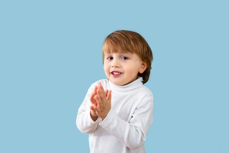 Portrait of little three years old boy clapping his hands. Smiling child applauds looking at the camera, isolated on light blue background, copy space.の写真素材