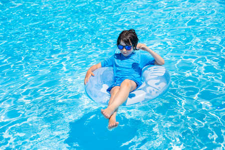 Young boy of nine years old resting on an inflatable ring in the swimming pool in summer. Child wearing sun protection tshirt and sun glasses enjoys holidays.の写真素材