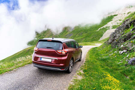 Dark red hatchback family car on serpantine road high in the mountains in France in rainy weather....