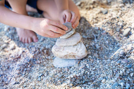 Child building a pile of stones on beach.Playing and relaxation at sea. Stone cairn on natural background. Concept balance.の写真素材