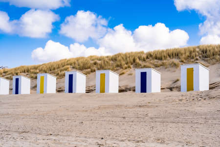 Little beach cabins at a North Sea. White little houses on the deserted sand dunes of Netherlands with blue cloudy sky.の写真素材