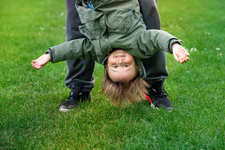 Father playing with little son outdoors on a grass. Toddler boy swinging upside down. Happy child in a park. Active parenting concept.の写真素材