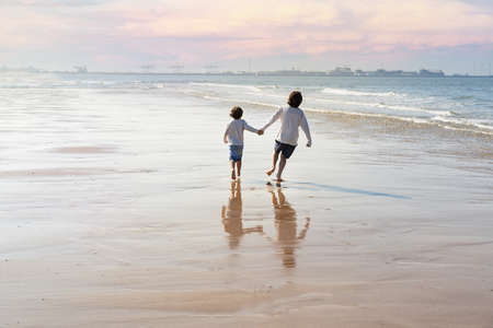 Two happy brothers holding hands are running along the seashore at the North Sea. Boys spending weekend at the seaside in Belgium, Knokke. Siblings friendship concept.の写真素材