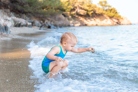 Little toddler boy wearing sun protection swimsuit playing with water at the sea side during summer vacation in Europe. Child enjoying sea. Family holidays concept.の写真素材