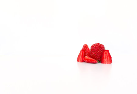 five pieces of red ripe strawberries cut into pieces on a white background with a slight reflection...