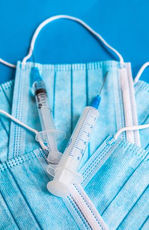 Two syringes on blue face medical mask on blue background. Medicine theme, healthcare. Copy spaceの写真素材
