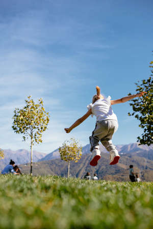 Happy little girl jumping with joy against blue sky in a sunny day, back view. High quality photoの写真素材