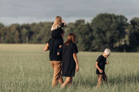 Family of four walking in field grass, enjoying nature and sunlight. Concept of lovely family spending time together. Back view. High quality photoの写真素材