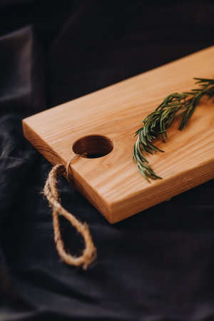 Cooking background concept. Close view of wooden cutting board with rosemary on dark background....