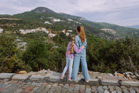 Two sisters hugging and looking at mountains on a cloudy day, back view. High quality photoの写真素材