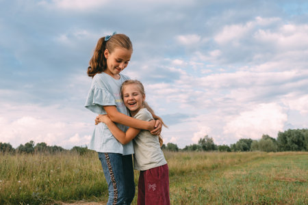 Two sisters hugging and smiling in a field under blue sky. High quality photoの写真素材