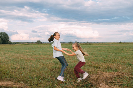 Two sisters spinning around and having fun in summer meadow under cloudy sky, two girls having fun in countryside in field, happy childhood concept. High quality photoの写真素材