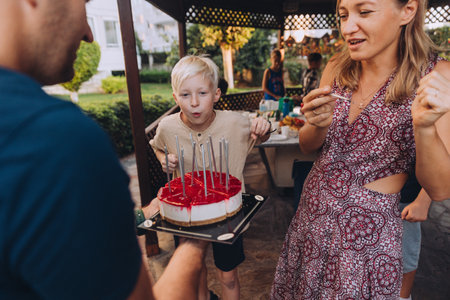 Happy Birthday cake for a young white haired boy, parents holding cake and their son blowing out candles on it, birthday party in family. High quality photoの写真素材