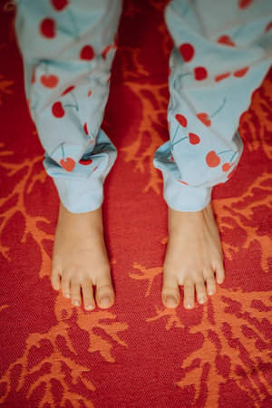 Top view of Childs feet barefoot in cute dotted pyjama pants standing on colourful orange rug. High quality photoの写真素材