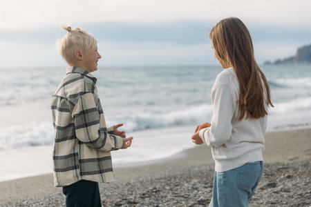 Happy adorable white haired boy talking to his girl friend at the beach, teen age friends having fun at seaside. High quality photoの写真素材