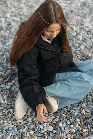 Sad and lonely Girl in black jacket sitting on gravy beach with her had down thinking. High quality photoの写真素材