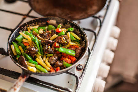 Red meat and colorful vegetables cooking in an old dirty fry pan, steam rising in a bright sunlight.の写真素材