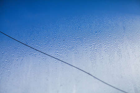 Water drops on a broken window glass on a blue cloudy sky backgroundの写真素材