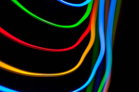 Colorful bright red, yellow, blue and green mixed Christmas lights flowing in various directions creating abstract movement on a black backgroundの写真素材