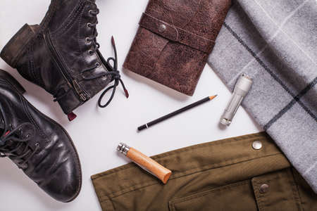 Wanderlust flatlay composition consisting of khaki jacket, grey scarf, leather notepad, pencil,...