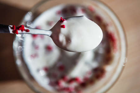 Spoon full of white yogurt with freeze dried raspberries above a bowlの写真素材