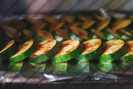 Picture of cut dark green zucchini covered with spices in process of baking inside electrical oven.の写真素材