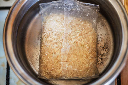 Plastic satchet of brown rice in process of cooking in boiling water in an old stainless steel...