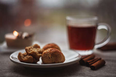 Three little curd and oatmeal buns with a cup of black tea, one bun broken in two pieces showing...