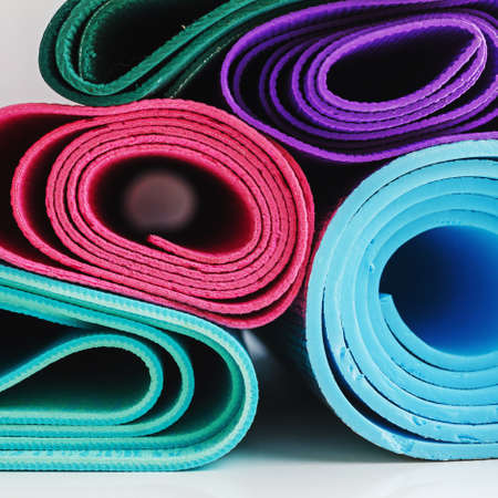 Stacked yoga mats of various bright colors, fitness themed background in a square frameの写真素材