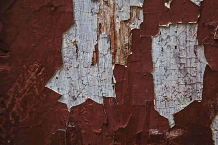Old chapped off red paint uncovering white paint layer on wooden surface