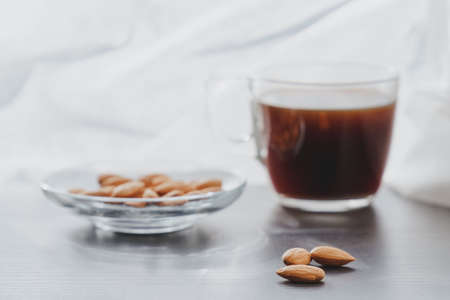 Concept of helathy snack - almonds with coffee placed on a dark laminate wood surface with white curtain on background on a very sunny dayの写真素材