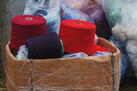 A bunch of big colorful thread spools in old carton box placed on the ground outdoors, transparent...