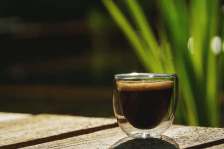 Small transparent double wall glass cup of fresh brewed coffee placed on a natural rough wooden...