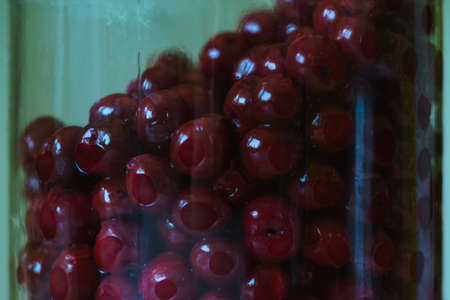 Closeup photo of alcohol soaked cherries in a big glass jar