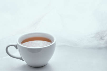 Simple white cup filled with tea on the left on white background