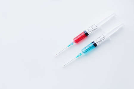 Two syringes filled with blue and red liquids on white background placed diagonally