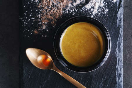 Beautiful photo of golden creamy skincare product in big elegant black glass jar near golden spoon...