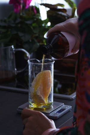Hand pouring seed oil on piece of plant butter in glass flask on weighing scale, preparing diy...
