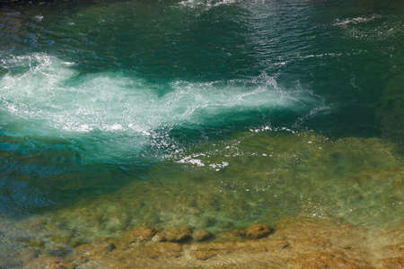 Deep turquoise color water flow filled with bubbles of air moving to surface near waterfal