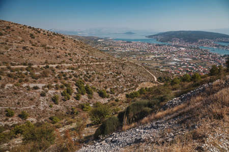 Beautiful sunny picture of city full of small houses with red roofs laying by the sea between high hills and mountainsの写真素材