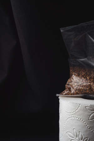 Vertical image of toilet paper roll and a sack of buckwheat on rough black cloth background