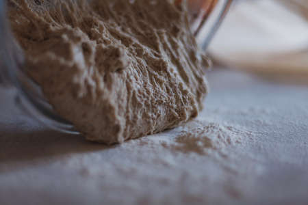 Close up of dough falling out of bowl onto table surface covered with flour