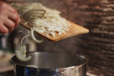 Process of placing fresh sliced onions into stainless steel cooking pot filled with boiling...