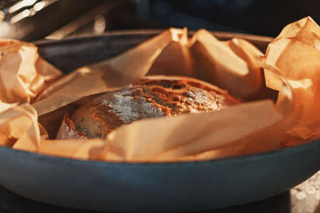 Freshly baked loaf of homemade bread wrapped in baking paper inside steel baking trayの写真素材