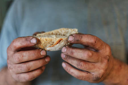 Piece of freshly baked bread in dirty hands of hard working man. Concept of earning your daily food by real work.の写真素材