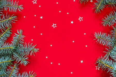 Frame made of blue Christmas tree branches and silver star shaped confetti on a red background. Top view, copy space, place for text.の写真素材