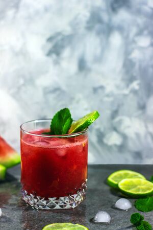 Watermelon smoothie with lime slices, mint and ice on gray background. Cold refreshing summer drink. Copy space, place for text.の写真素材
